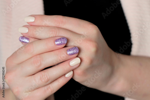two hands with nude manicure and purple glitter design