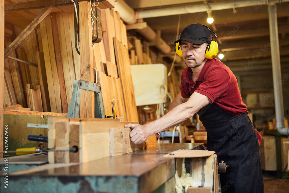 Senior carpenter in uniform works on a woodworking machine at the carpentry manufacturing Senior carpenter in uniform works on a woodworking machine at the carpentry manufacturing