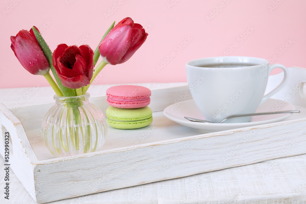 Tulips in glass vase, macaroons and cup of coffee or tea on white wooden tray