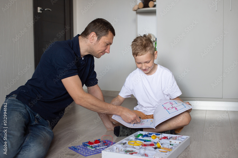 A cute boy in a white T-shirt collects an electrical designer with his dad in the room A cute boy in a white T-shirt collects an electrical designer with his dad in the room