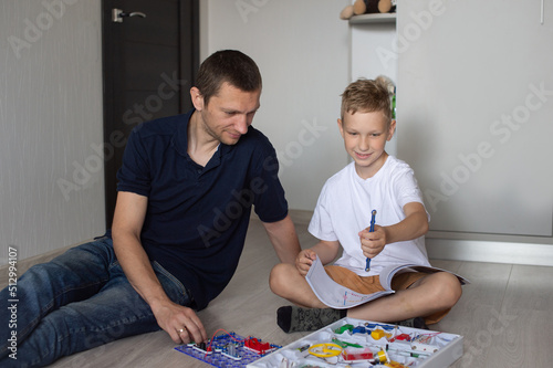 A cute boy in a white T-shirt collects an electrical designer with his dad in the room