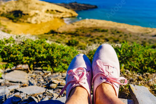 Female legs in sneakers against coast landscape, Spain.