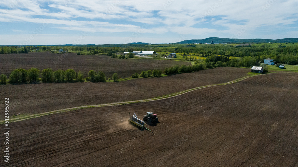 Aerial view of a tractor baling hay in a field in spring in quebec canada