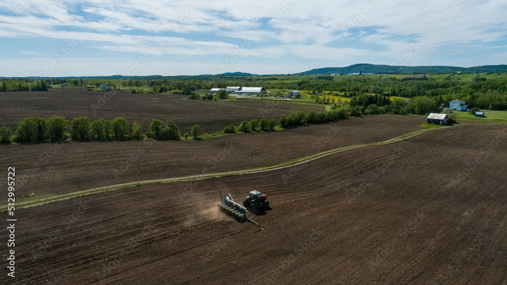 Obraz premium Aerial view of a tractor baling hay in a field in spring in quebec canada