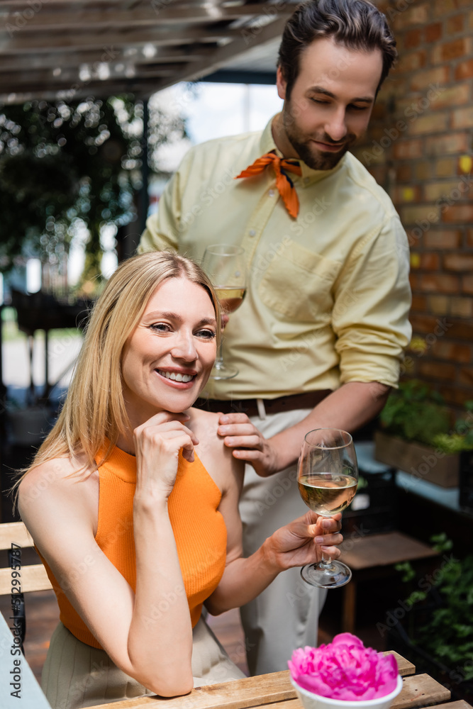 Smiling woman holding glass of wine near stylish boyfriend in outdoor cafe.