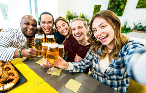 Happy multiracial friends drinking beer at brewery pub - Young people taking selfie dining sitting at bar restaurant table - Youth lifestyle and beverage concept