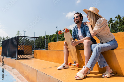 Positive couple with longboard sitting in skate park. photo