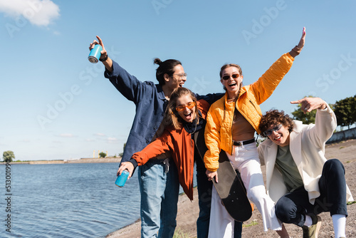 happy man showing rock sign near multicultural friends with skateboard and soda cans.