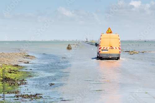 Véhicule d'entretien avec panneau travaux s'engageant sur une route submergée entre une île et le continent. Passage du Gois, Noirmoutier