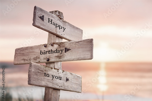 happy birthday to you text quote on wooden crossroad signpost outdoors on beach with pink pastel sunset colors. Romantic theme.