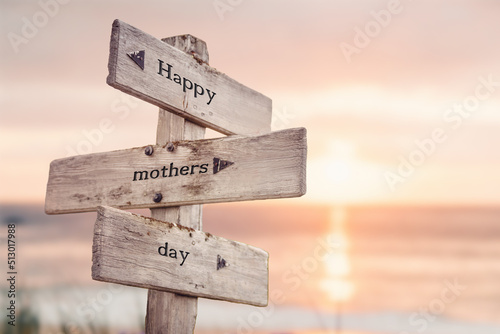 happy mothers day text quote on wooden crossroad signpost outdoors on beach with pink pastel sunset colors. Romantic theme.