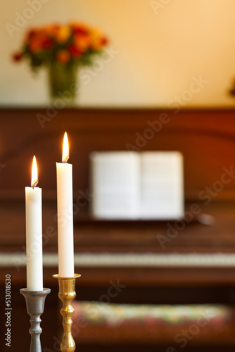 Two thin candles in candle stick holders burning against blurry piano and bouquet of flowers background. Elegant candle lights in gold and silver holders, for a wedding, funeral home or church