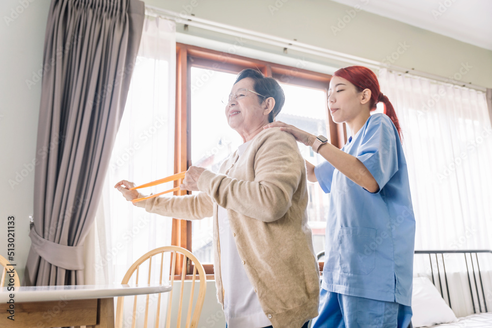 Nurse caregiver wearing scrubs exercises with a senior Asian woman by using resistance band exercise for the senior patient in physiotherapy treatment. Home health care and nursing home concept. Nurse caregiver wearing scrubs exercises with a senior Asian woman by using resistance band exercise for the senior patient in physiotherapy treatment. Home health care and nursing home concept.