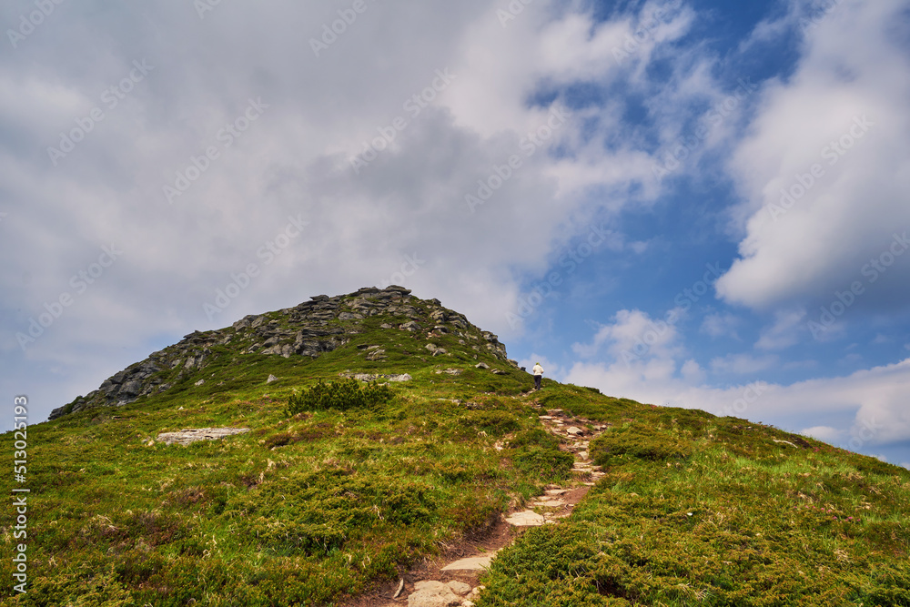 Girl tourist climbs the path to the top of the mountain. Beautiful mountain landscape with cloudy sky