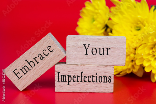 Embrace your imperfections text on wooden cube and with flowers background. photo