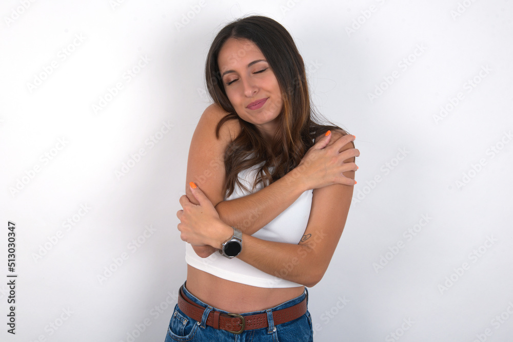 young beautiful caucasian woman wearing white top over white background. Hugging oneself happy and positive, smiling confident. Self love and self care. young beautiful caucasian woman wearing white top over white background. Hugging oneself happy and positive, smiling confident. Self love and self care.