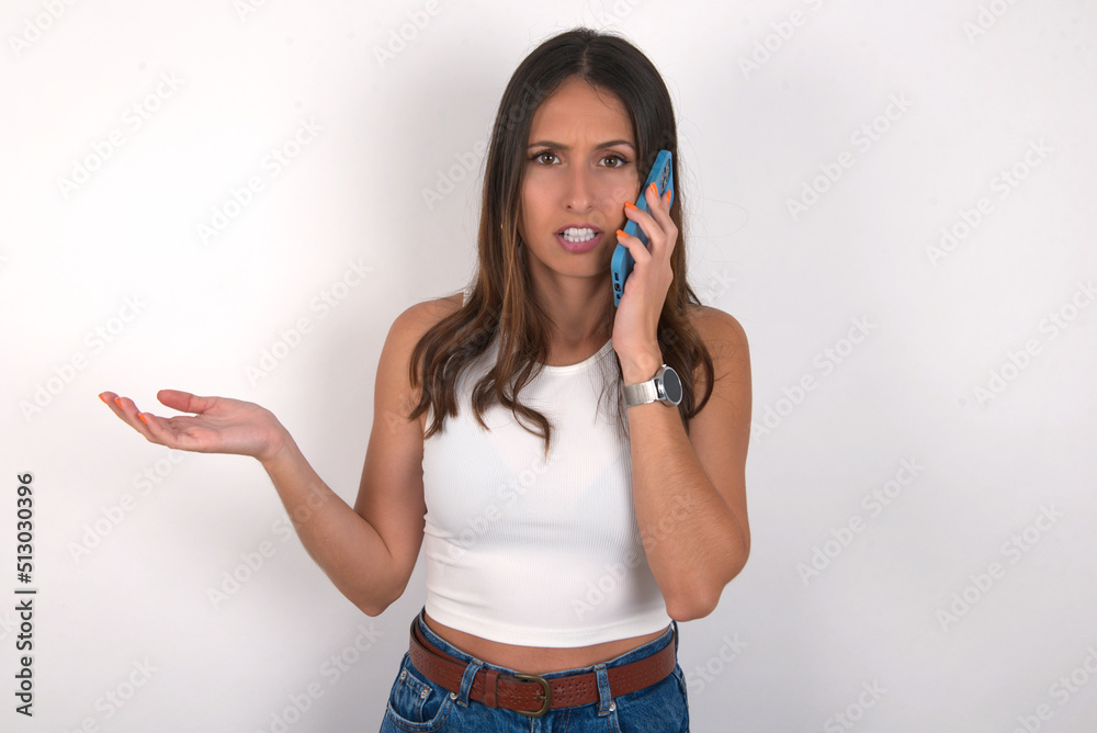 young beautiful caucasian woman wearing white Top over white talking on the phone stressed with hand on face, shocked with shame and surprise face, angry and frustrated. Fear and upset for mistake.