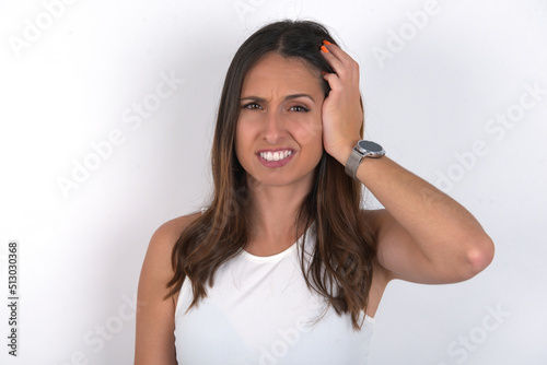 Portrait of confused young beautiful caucasian woman wearing white Top over white background holding hand on hair and frowning, panicking, losing memory. Worried and anxious can not remember anything. © Jihan