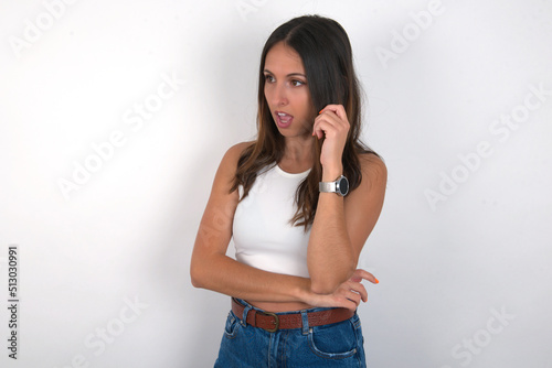 Astonished young beautiful caucasian woman wearing white Top over white background looks aside surprisingly with opened mouth. photo