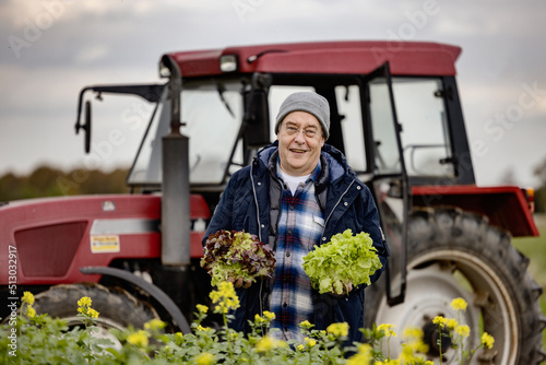 Bauer mit Salat in der Hand auf einem Feld vr seinem Traktor