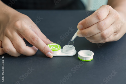 Girl takes contact lens out of container with tweezers. Black background, close-up, side view