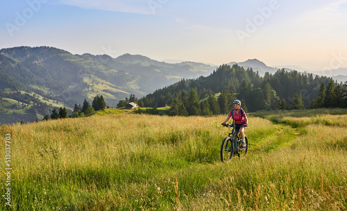 pretty senior woman riding her electric mountain bike on the mountains above Oberstaufen with Nagelfluh mountain chain in background, Allgau Alps, Bavaria Germany