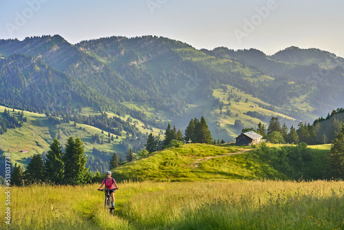 pretty senior woman riding her electric mountain bike on the mountains above Oberstaufen with Nagelfluh mountain chain in background, Allgau Alps, Bavaria Germany
