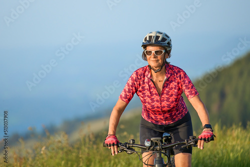 pretty senior woman riding her electric mountain bike on the mountains above Oberstaufen with Nagelfluh mountain chain in background, Allgau Alps, Bavaria Germany