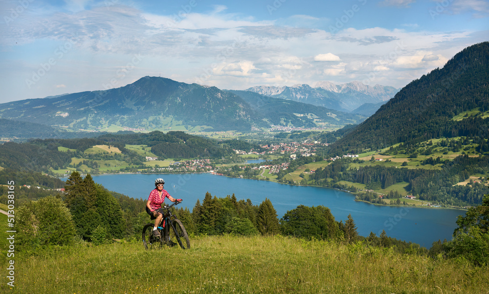 beautiful senior woman riding her electric mountain bike  on the mountains above Lake Alpsee near Immenstadt, Allgau,Bavaria, Germany
