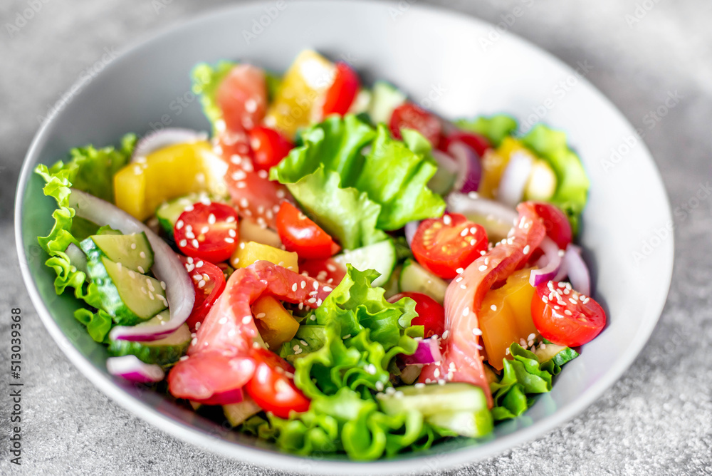 Salted salmon salad with fresh green lettuce, cucumbers, tomatoes, sweet peppers and red onions on a stone background. Ketogenic, keto or paleo diet lunch bowl.