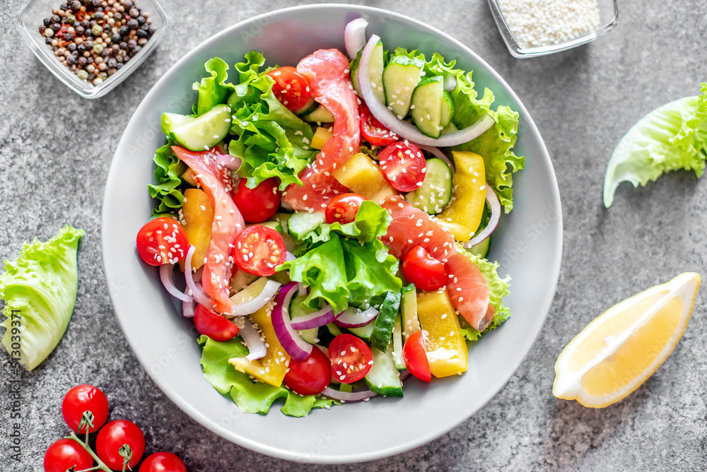 Salted salmon salad with fresh green lettuce, cucumbers, tomatoes, sweet peppers and red onions on a stone background. Ketogenic, keto or paleo diet lunch bowl.