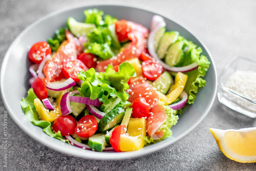 Salted salmon salad with fresh green lettuce, cucumbers, tomatoes, sweet peppers and red onions on a stone background. Ketogenic, keto or paleo diet lunch bowl.