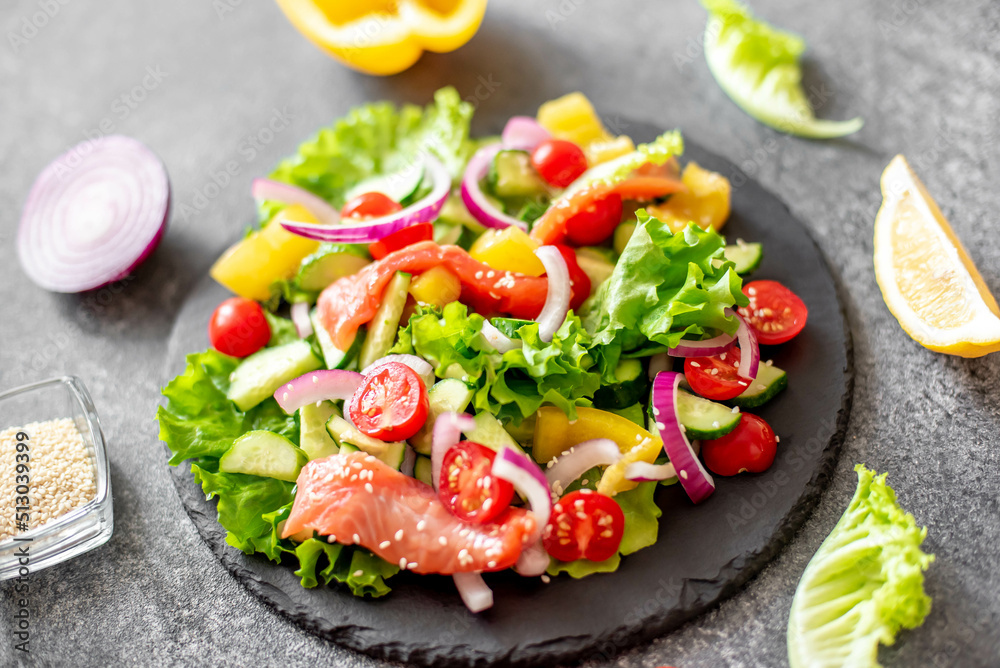 Salted salmon salad with fresh green lettuce, cucumbers, tomatoes, sweet peppers and red onions on a stone background 