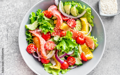 Salted salmon salad with fresh green lettuce, cucumbers, tomatoes, sweet peppers and red onions on a stone background. Ketogenic, keto or paleo diet lunch bowl.