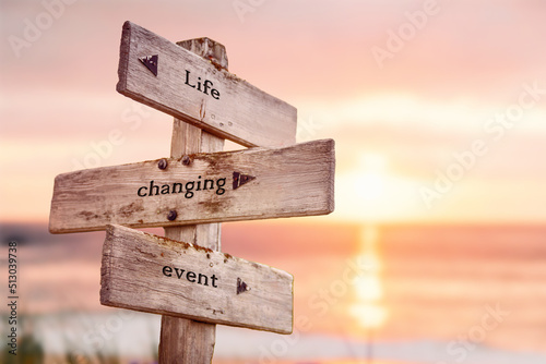 life changing event text quote on wooden crossroad signpost outdoors on beach with pink pastel sunset colors. Romantic theme. photo