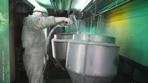 Industrial painting process in chamber. Painter spraying green paint on detail in special booth. Technician in safety wear work at industrial manufacture. Master paint parts in specialised workshop photo