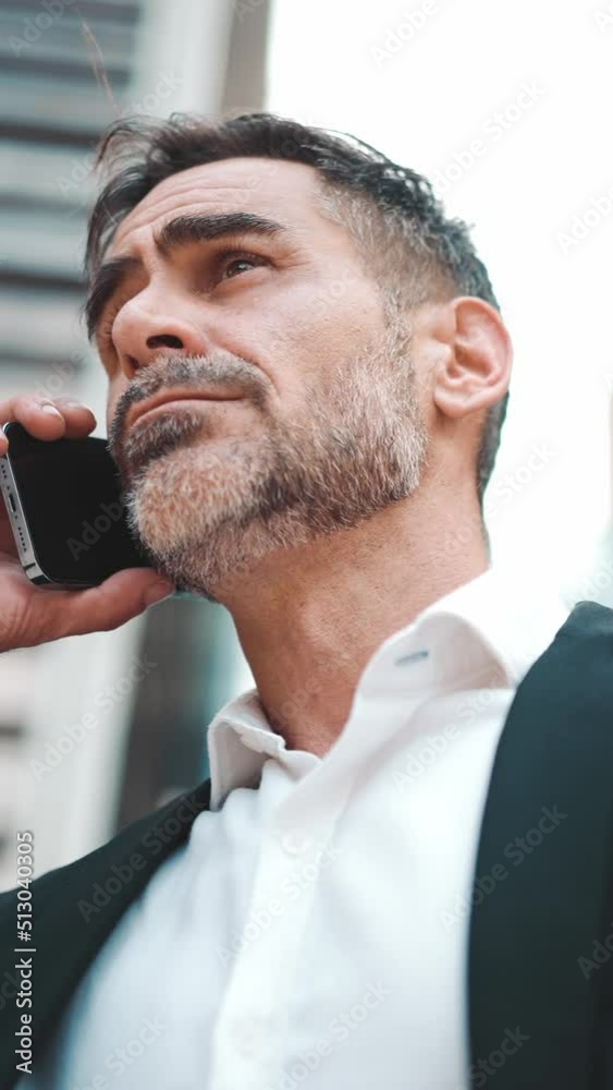 Middle-aged businessman with neat beard in office clothes uses mobile phone. Successful man emotionally talking on smartphone. Camera moves around Middle-aged businessman with neat beard in office clothes uses mobile phone. Successful man emotionally talking on smartphone. Camera moves around