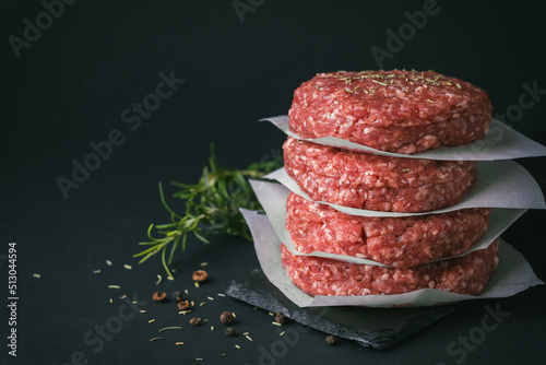 Raw ground beef burger patties separated by baking paper on a black background
