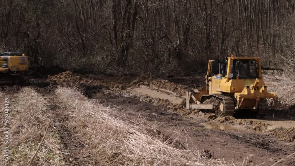 Bulldozer at construction site shovels soil into heap. Construction equipment. Heavy yellow excavator with folded boom. Excavator heavy machinery for industrial company. Bulldozer at construction site shovels soil into heap. Construction equipment. Heavy yellow excavator with folded boom. Excavator heavy machinery for industrial company.