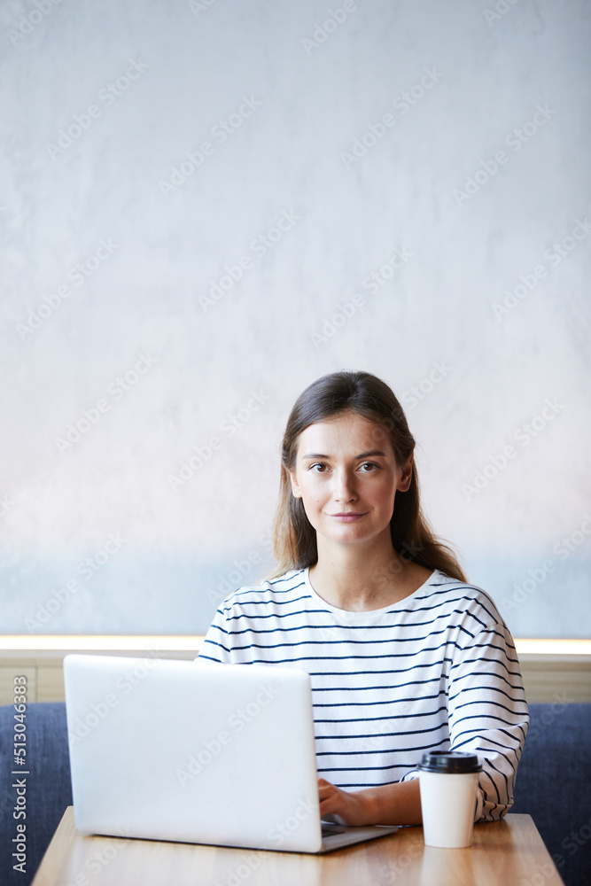 Portrait of content confident young freelancer in black and white stripped sweater sitting at table and working with laptop in cafe with wifi Portrait of content confident young freelancer in black and white stripped sweater sitting at table and working with laptop in cafe with wifi
