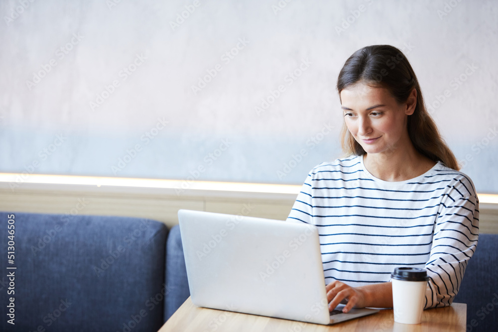 Content busy young woman in casual sweater sitting at table in coffee shop and checking mail on laptop Content busy young woman in casual sweater sitting at table in coffee shop and checking mail on laptop