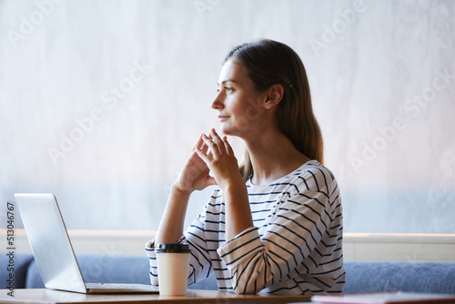 Introspective purposeful young lady sitting at table in modern cafe and thinking of new internet project