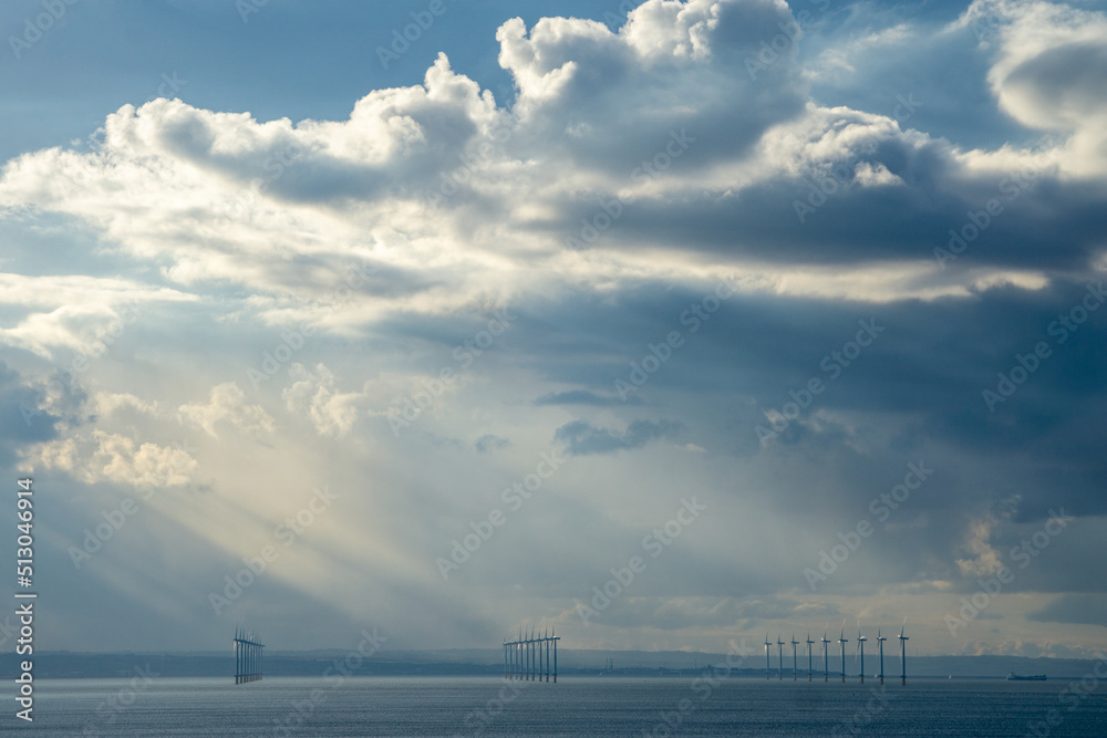 The Sun burst through a dramatic sky lighting an offshore Wind farm near Redcar from Saltburn