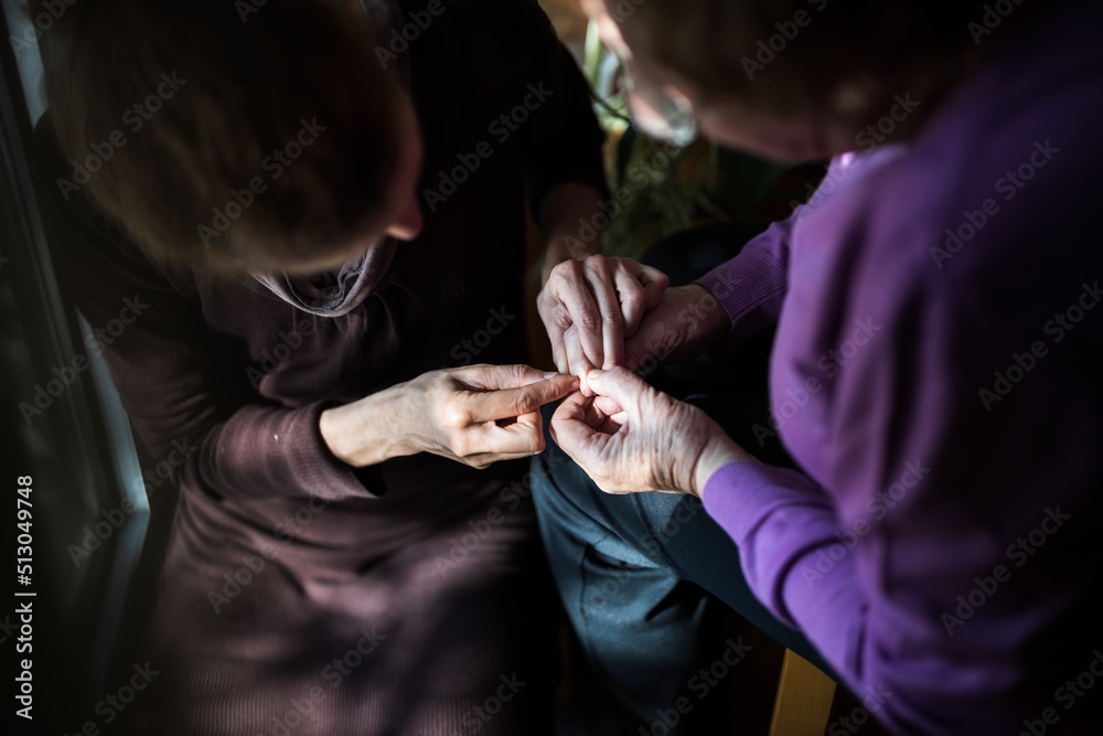 Obraz premium Mid Adult Woman Care Giver Helps Senior Woman to Remove some Thorns from Her Hands at Window better Light in Domestic Environment