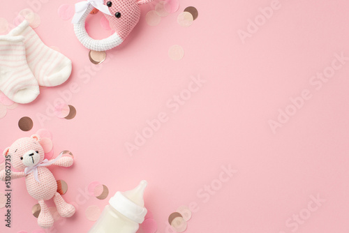 Baby girl concept. Top view photo of tiny socks knitted bunny rattle toy teddy-bear toy milk bottle and shiny confetti on isolated pastel pink background with copyspace