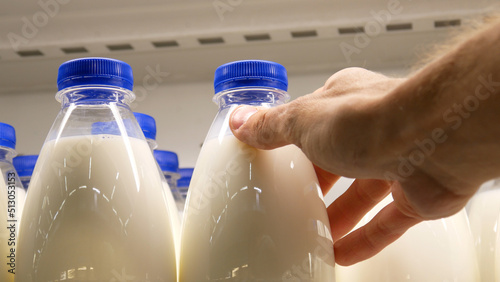 Obraz na plátně Close-up of many plastic milk bottles with blue caps and a male buyer's hand tak