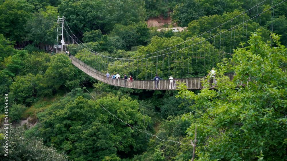 People Walking Along Suspension Bridge in Picturesque Green Forest Setting. Khnodzersk bridge in Armenia. Surround by Rich Green Trees. High quality 4k footage People Walking Along Suspension Bridge in Picturesque Green Forest Setting. Khnodzersk bridge in Armenia. Surround by Rich Green Trees. High quality 4k footage