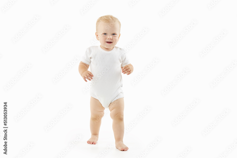 Cute baby learns to walk on a white isolated background. Happy smiling child in white clothes makes first confident steps Cute baby learns to walk on a white isolated background. Happy smiling child in white clothes makes first confident steps