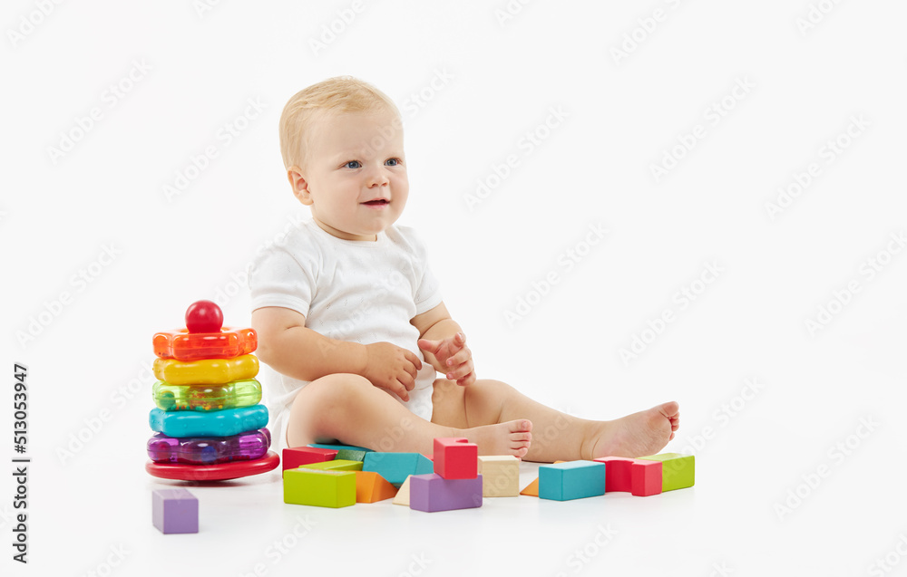 Cute baby plays with toys on a white isolated background. The child folds a constructor and a pyramid Cute baby plays with toys on a white isolated background. The child folds a constructor and a pyramid