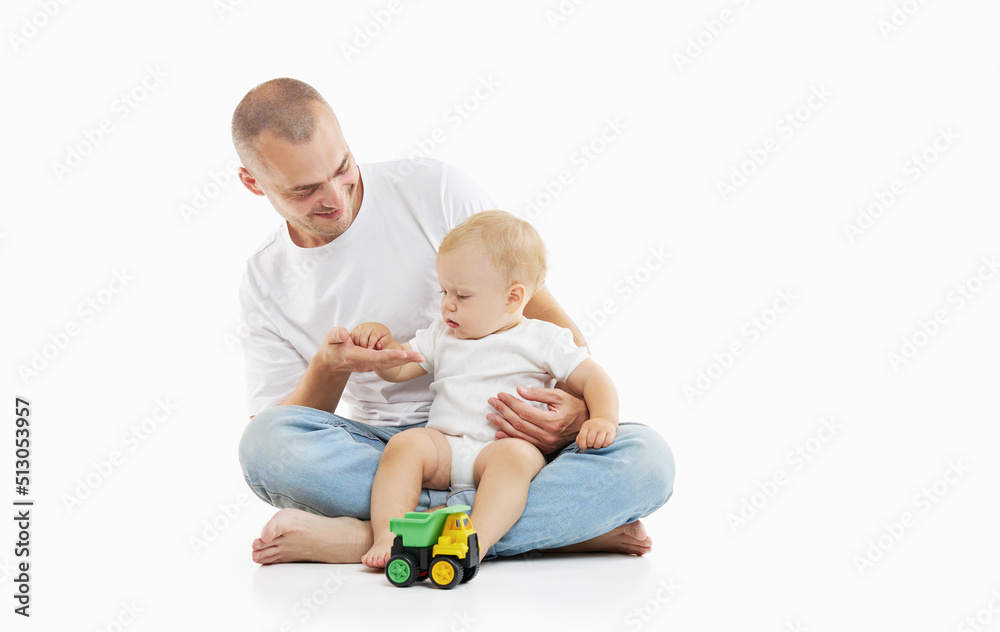 A young dad plays with a baby on a light studio background. Family values